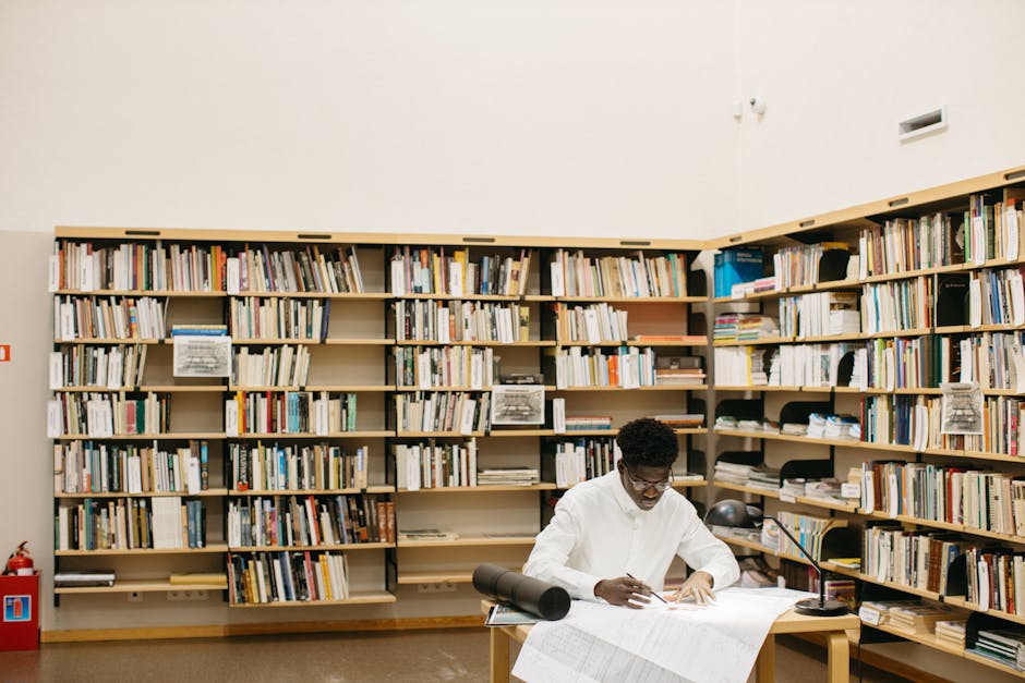 A focused architect working on blueprints in a tranquil library filled with books.